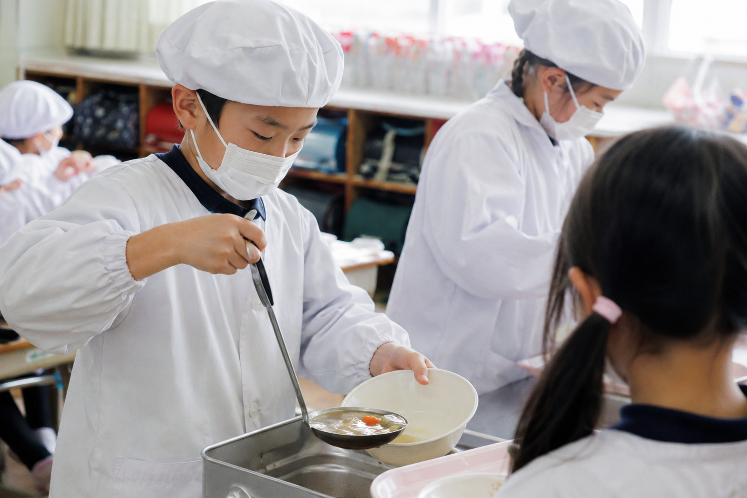 給食当番表 作り方 給食当番の白衣を着て配膳する小学生