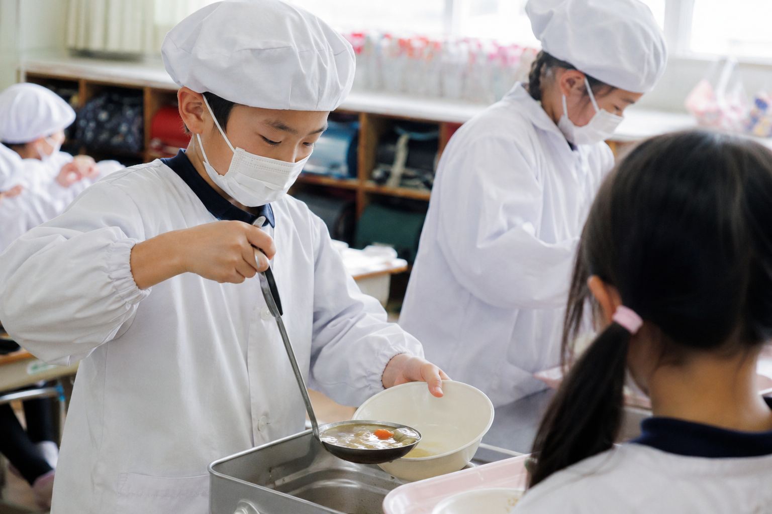 給食当番表 作り方 給食当番の白衣を着て配膳する小学生